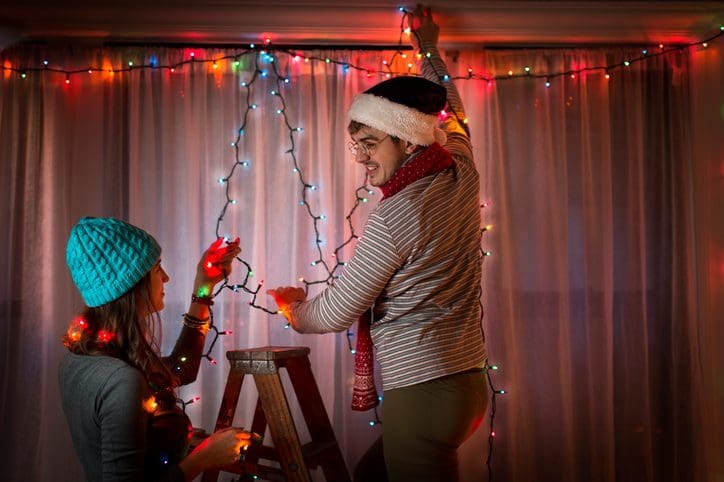 Gill Insurance | Young couple putting up fairy lights at christmas