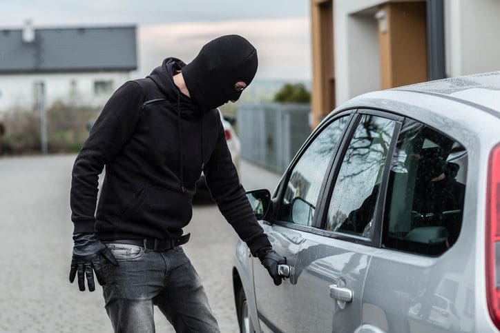 Gill Insurance | Man dressed in black with a balaclava on his head pulls the handle of a car. Car thief, car theft concept