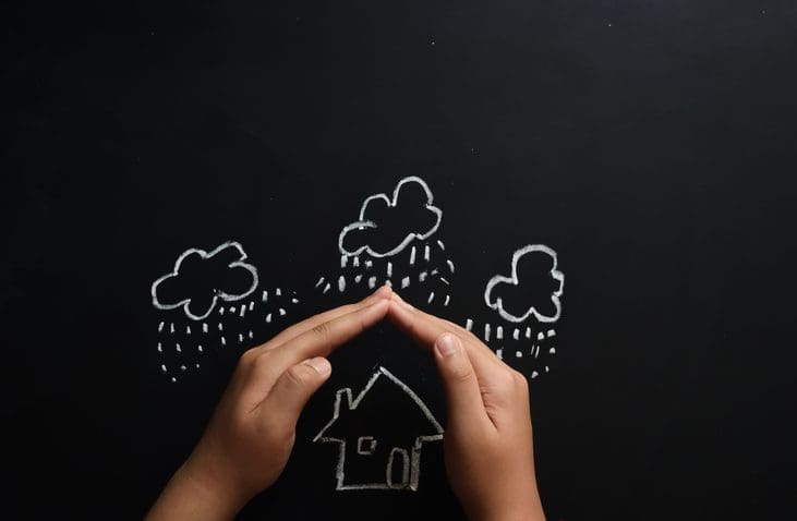 Gill Insurance | Home insurance concept child protecting house by his hands. Child protecting drawn house on black board from rain and thunder. No human face included in the photograph. You could add your texts on the black copy space. Perfect image for home insurance company, home maintenance