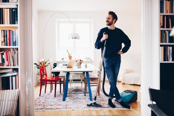 Gill Insurance | Happy man standing with vacuum cleaner in dining room at home
